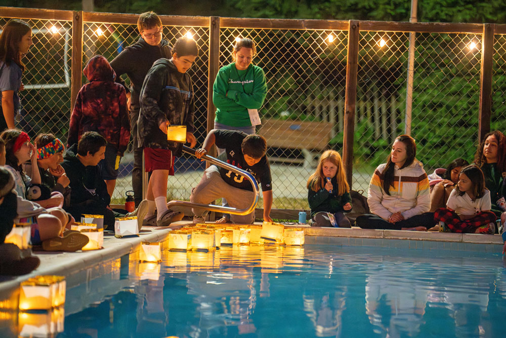 kids around a swimming pool putting lanterns in the pool at night