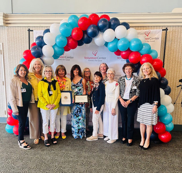 people standing and smiling in front of a volunteer center banner with balloons